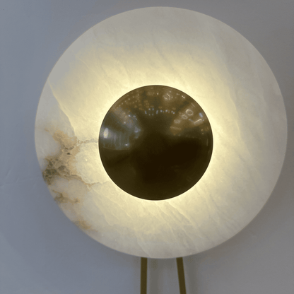 Close-up of alabaster lighting fixture with polished brass disc emitting soft light.