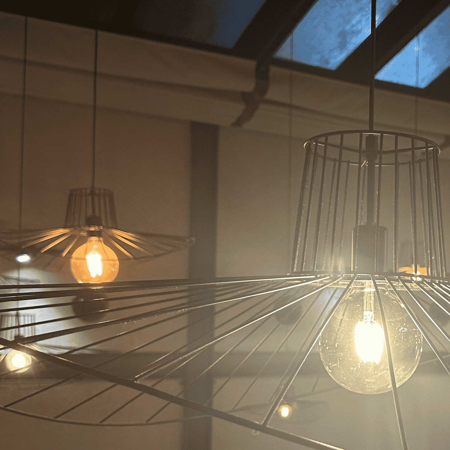 Straw hat pendant light with curved wire shade glowing near skylight in a modern interior.