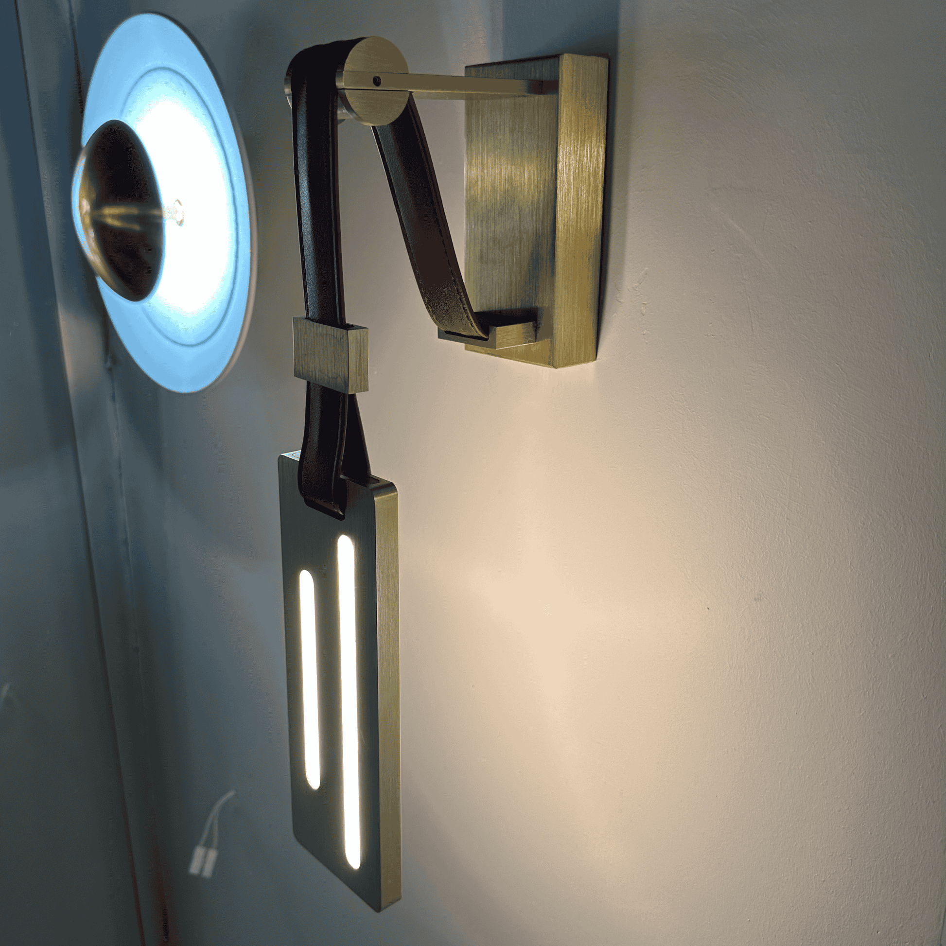Contemporary wall-mounted leather sconce with brass arm and vertical LED lighting.