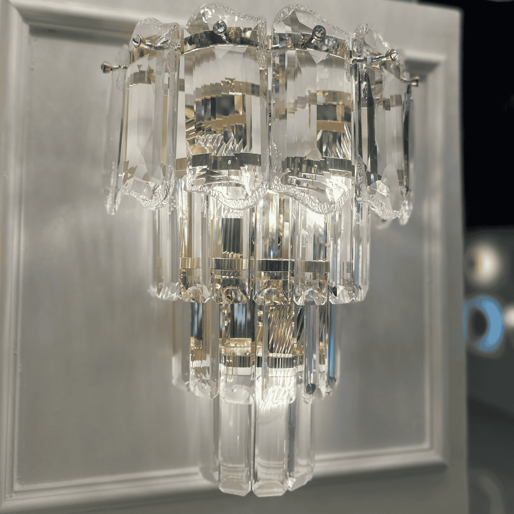 Modern crystal wall sconce light with faceted clear glass panels mounted on a neutral wall.