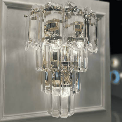 Modern crystal wall sconce light with faceted clear glass panels mounted on a neutral wall.