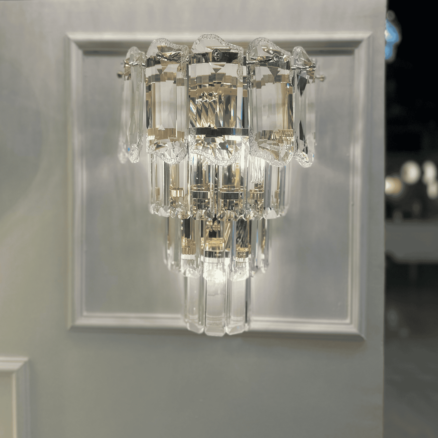 Contemporary crystal wall sconce light with a tiered clear glass structure and chrome base.
