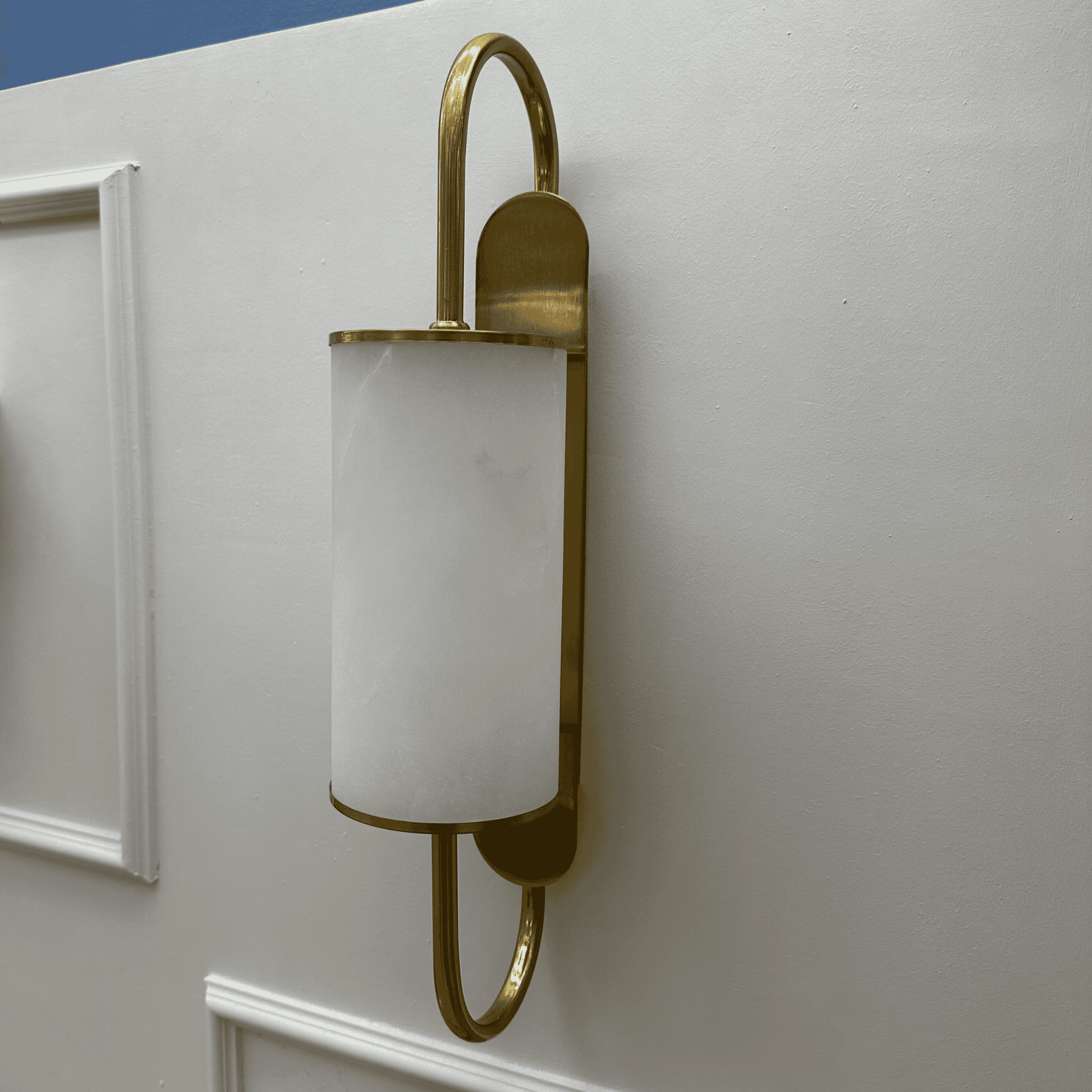 Wall-mounted brass sconce with a curved frame and alabaster shade against a light background.
