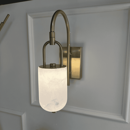 Close-up of curved brass marble wall sconce with glowing alabaster shade.