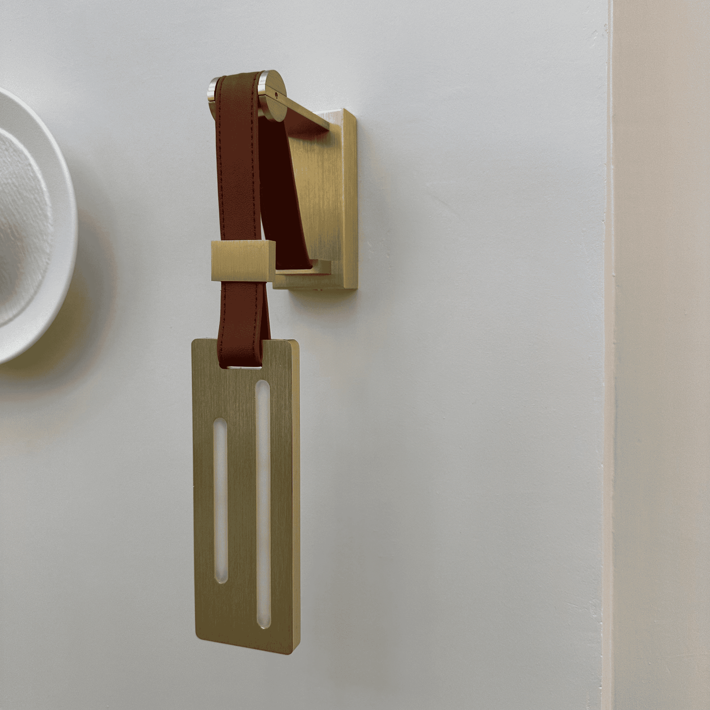 Designer leather wall sconce with brass bracket and vertical light cutouts.