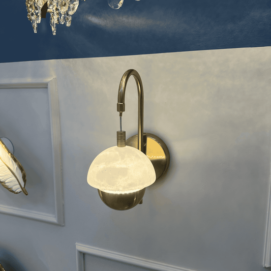 Brass and marble sconce glowing near a chandelier in a luxurious interior.