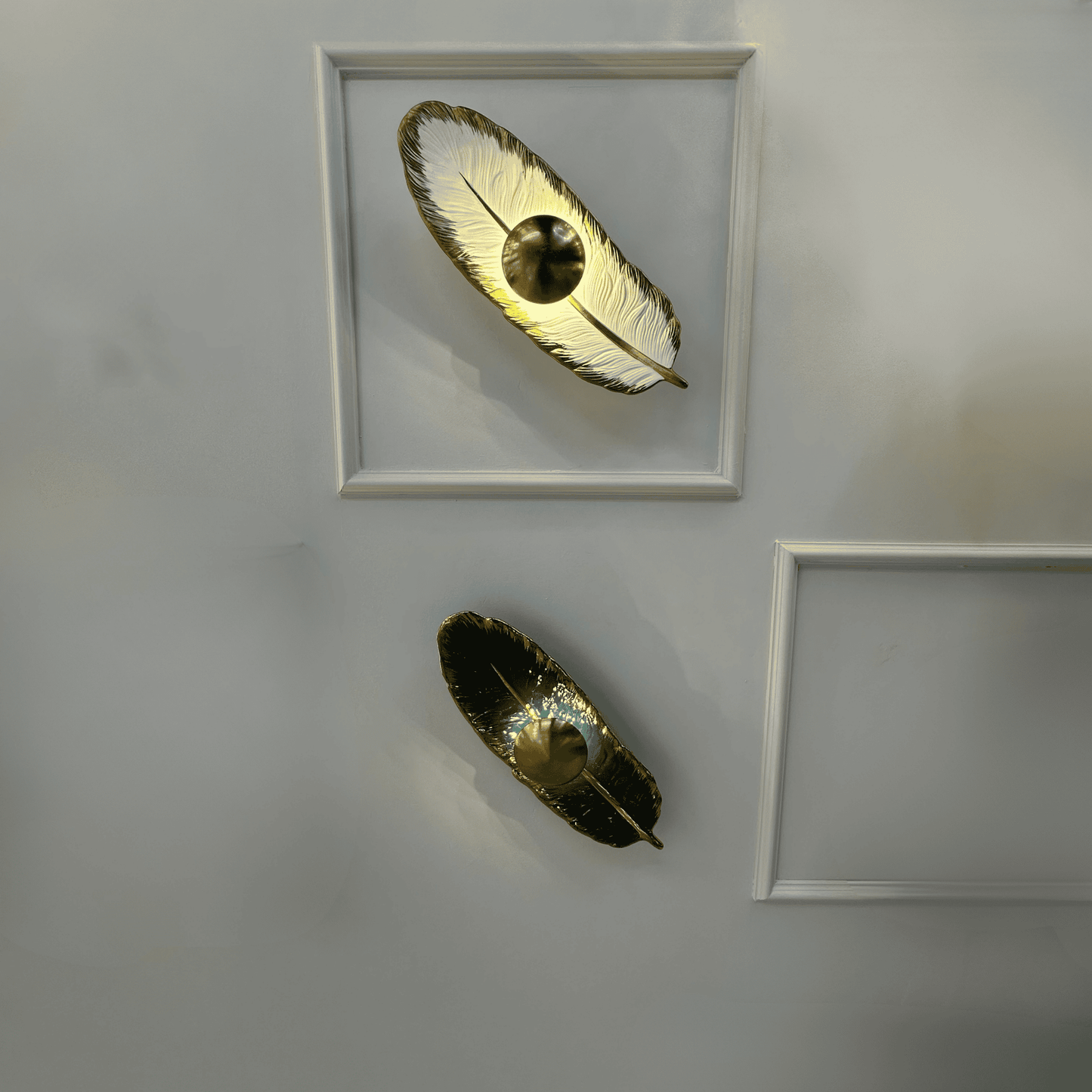 Dual feather wall lights with porcelain and brass finish feature integrated LED lighting, mounted on a paneled wall for contemporary interior lighting design.