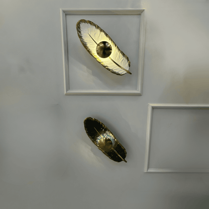 Dual feather wall lights with porcelain and brass finish feature integrated LED lighting, mounted on a paneled wall for contemporary interior lighting design.