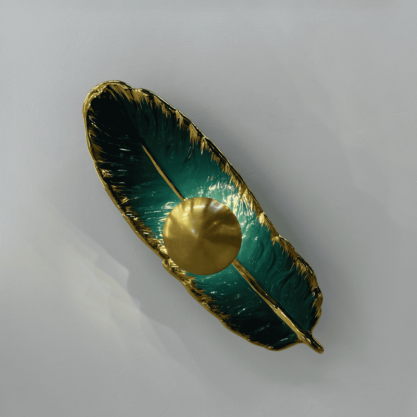 Horizontally placed feather wall light in emerald porcelain and brass finish with LED lighting, enhancing a contemporary interior wall.