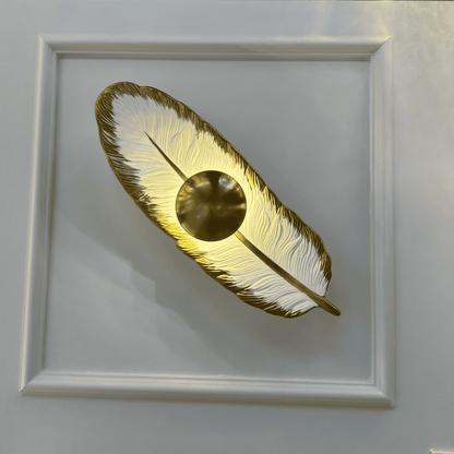 Porcelain feather wall light with a brass LED core glowing against a decorative paneled wall for ambient lighting.