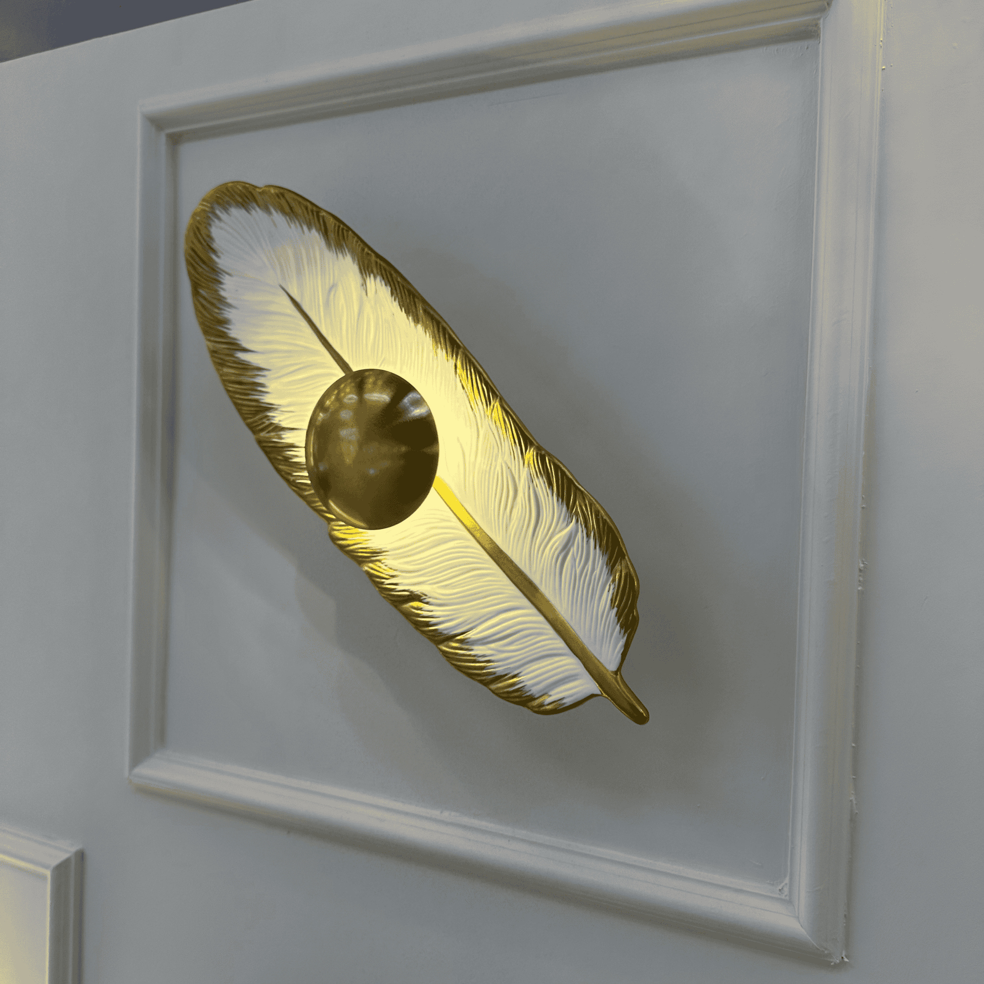 A porcelain and brass feather wall light with LED illumination mounted on a decorative paneled wall, viewed from an upper angle.