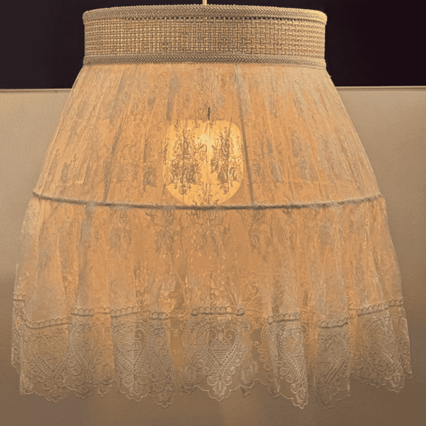 Illuminated close-up of lace pendant lamp with sheer embroidery and woven top, casting warm ambient glow.