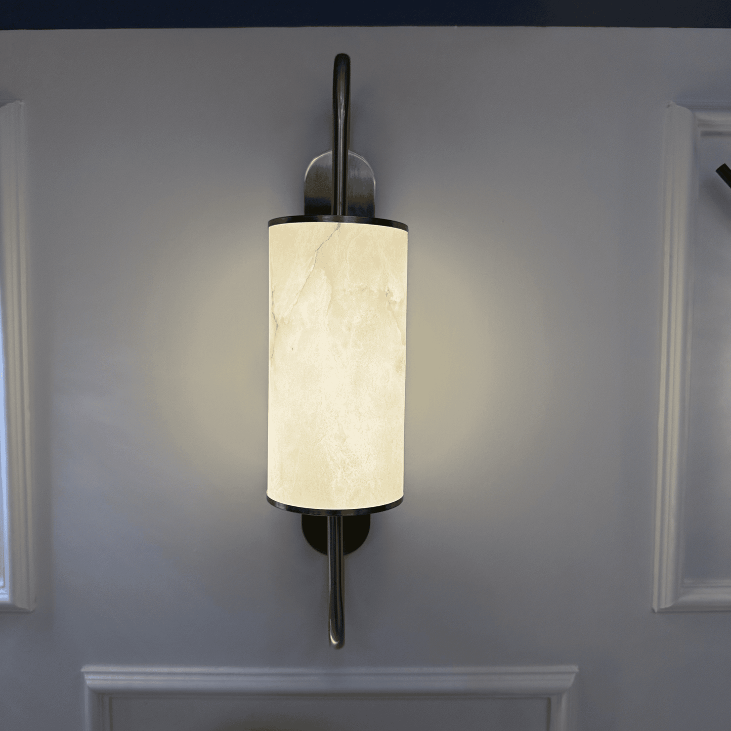 Glowing alabaster wall sconce with brass accents mounted on a white wall.