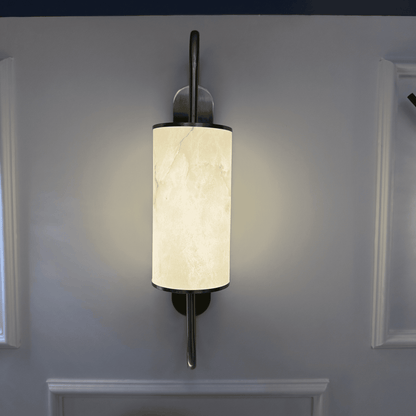 Glowing alabaster wall sconce with brass accents mounted on a white wall.