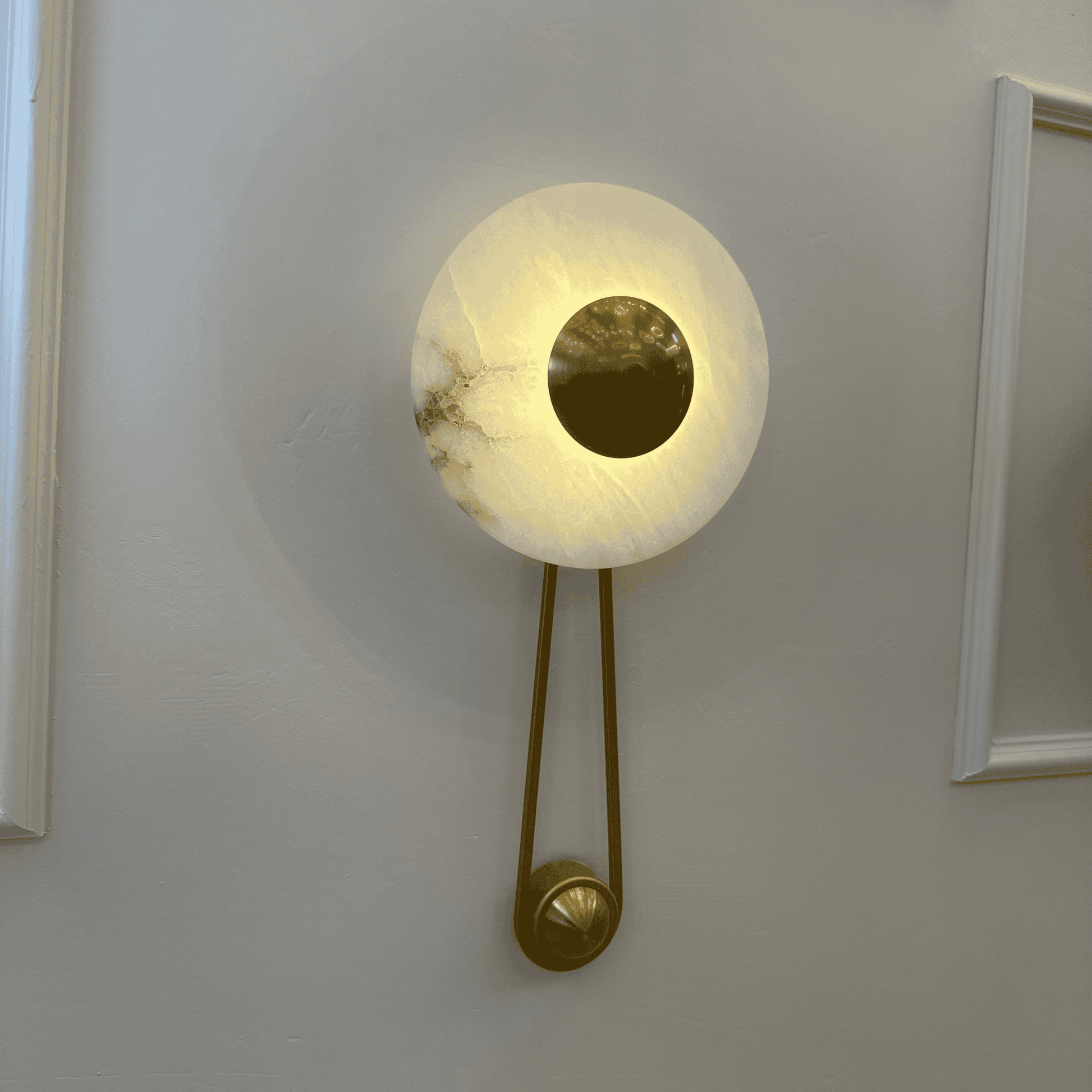 Softly lit alabaster wall light with a central round brass disc mounted on a pale wall.