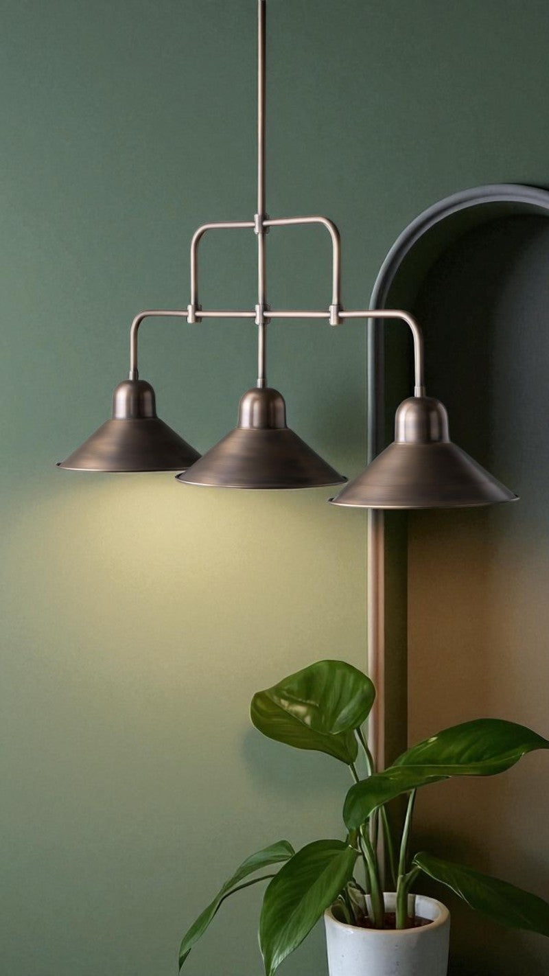 Bronze triple pendant light shines against a green wall, illuminating a potted plant in a modern interior.