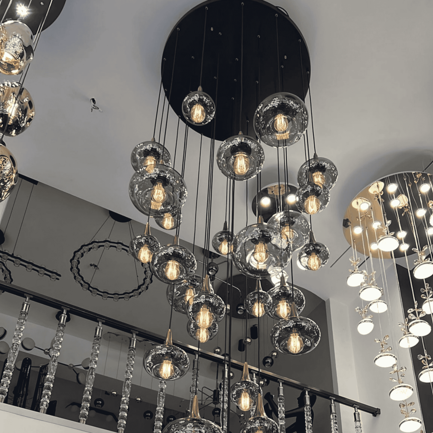 Large vertical installation of glass globe pendant lights suspended in tiers from a dark circular ceiling plate.