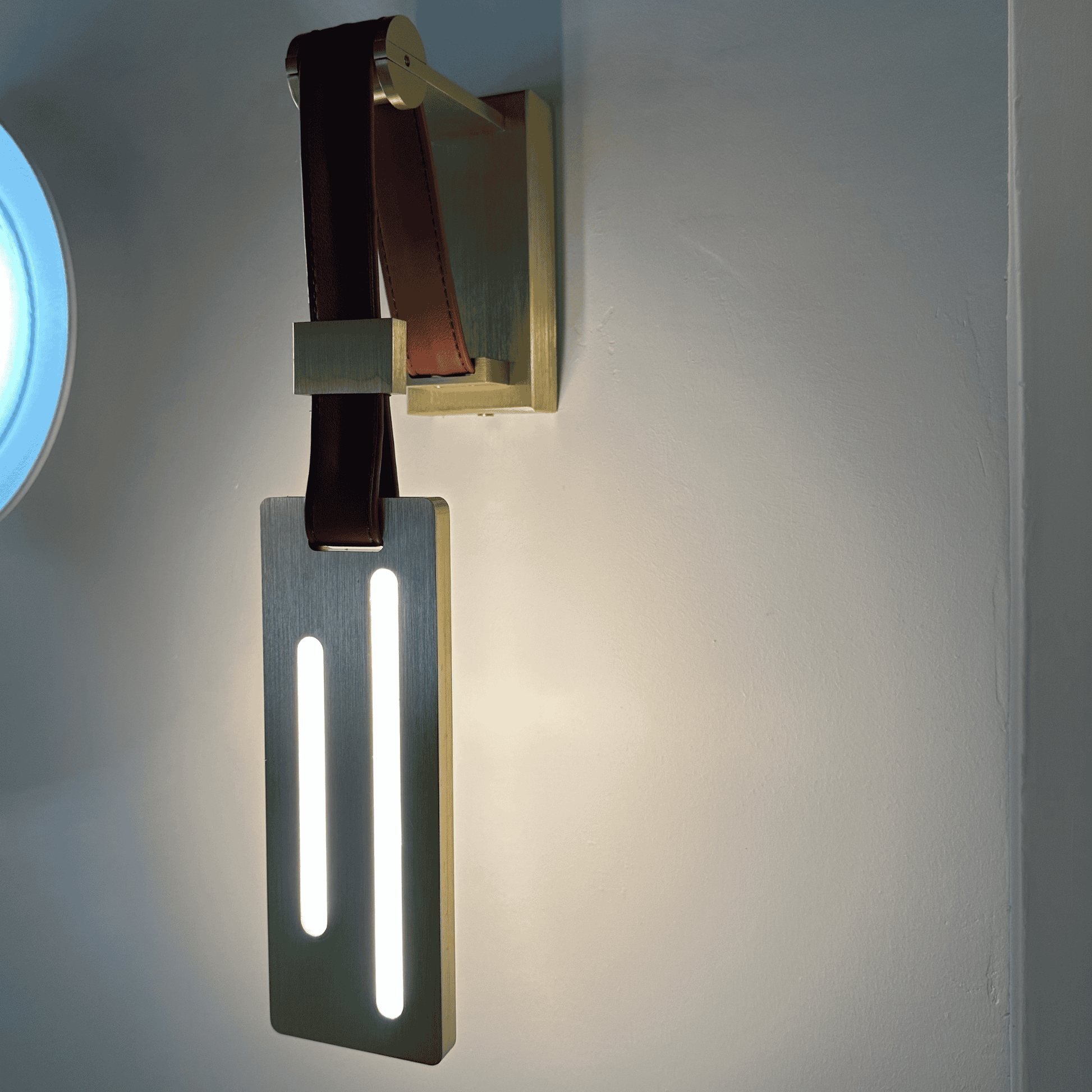 Dual vertical LED leather wall sconce with brushed brass base for luxury lighting decor.