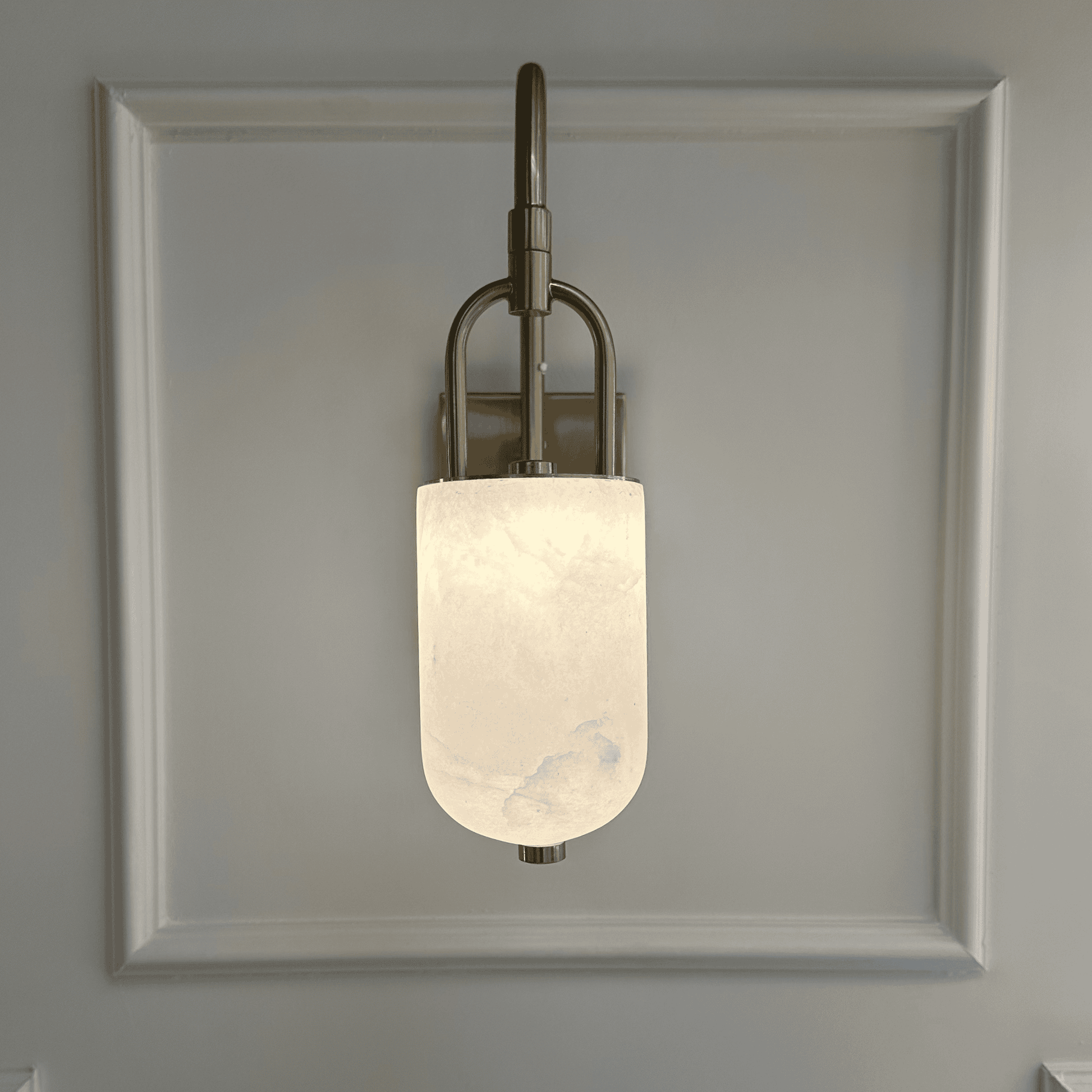 Arched brass and alabaster marble wall sconce emitting soft white glow.