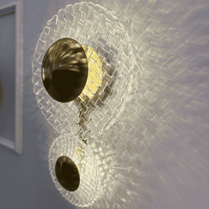 Close-up of luxury brass and clear glass wall sconce emitting patterned light across entryway wall.
