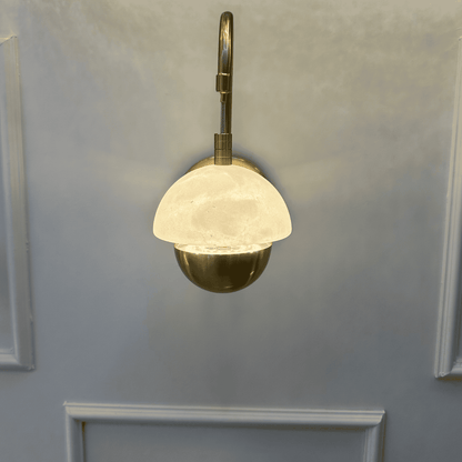 Modern marble sconce with brass fixture and dome-shaped shade mounted on a paneled wall.