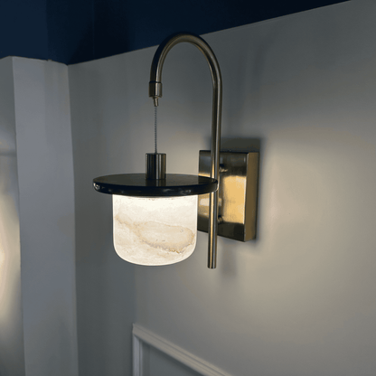 Marble sconce wall light with brass arm and alabaster shade on neutral wall.