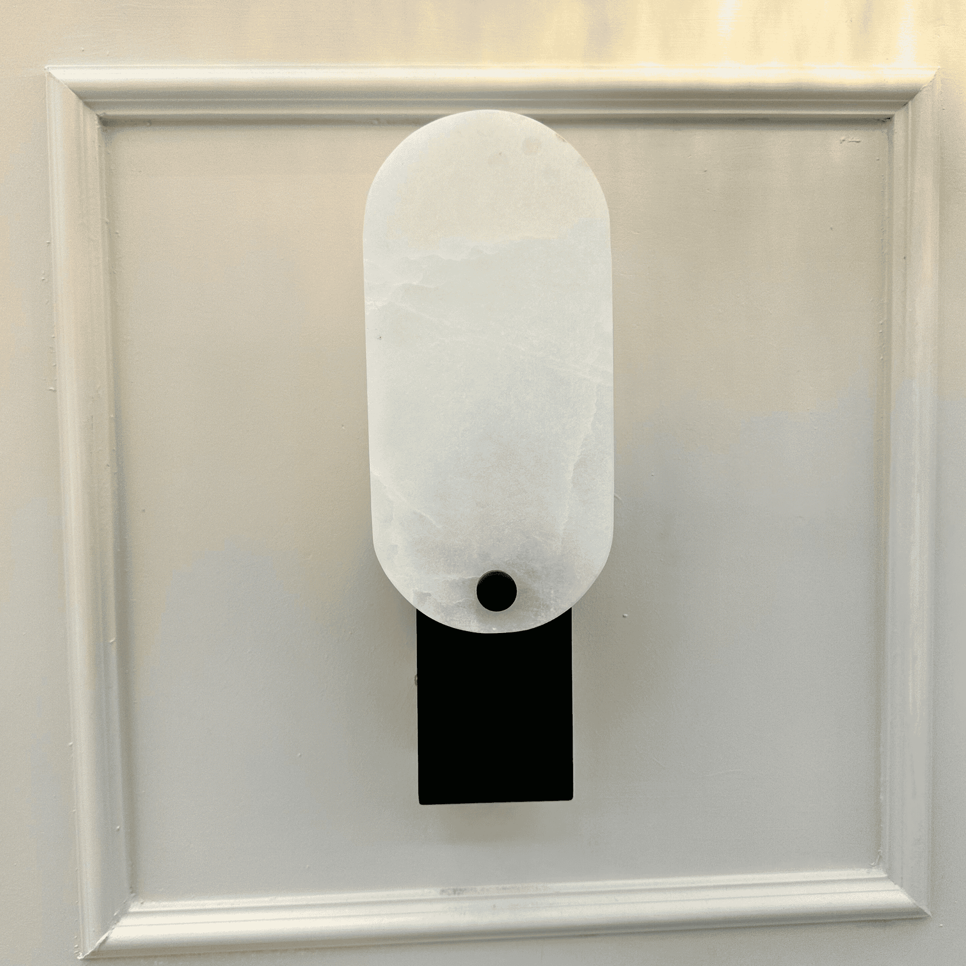 Matte black square marble wall light with white stone face mounted on decorative panel wall.