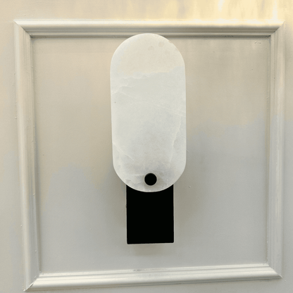 Matte black square marble wall light with white stone face mounted on decorative panel wall.