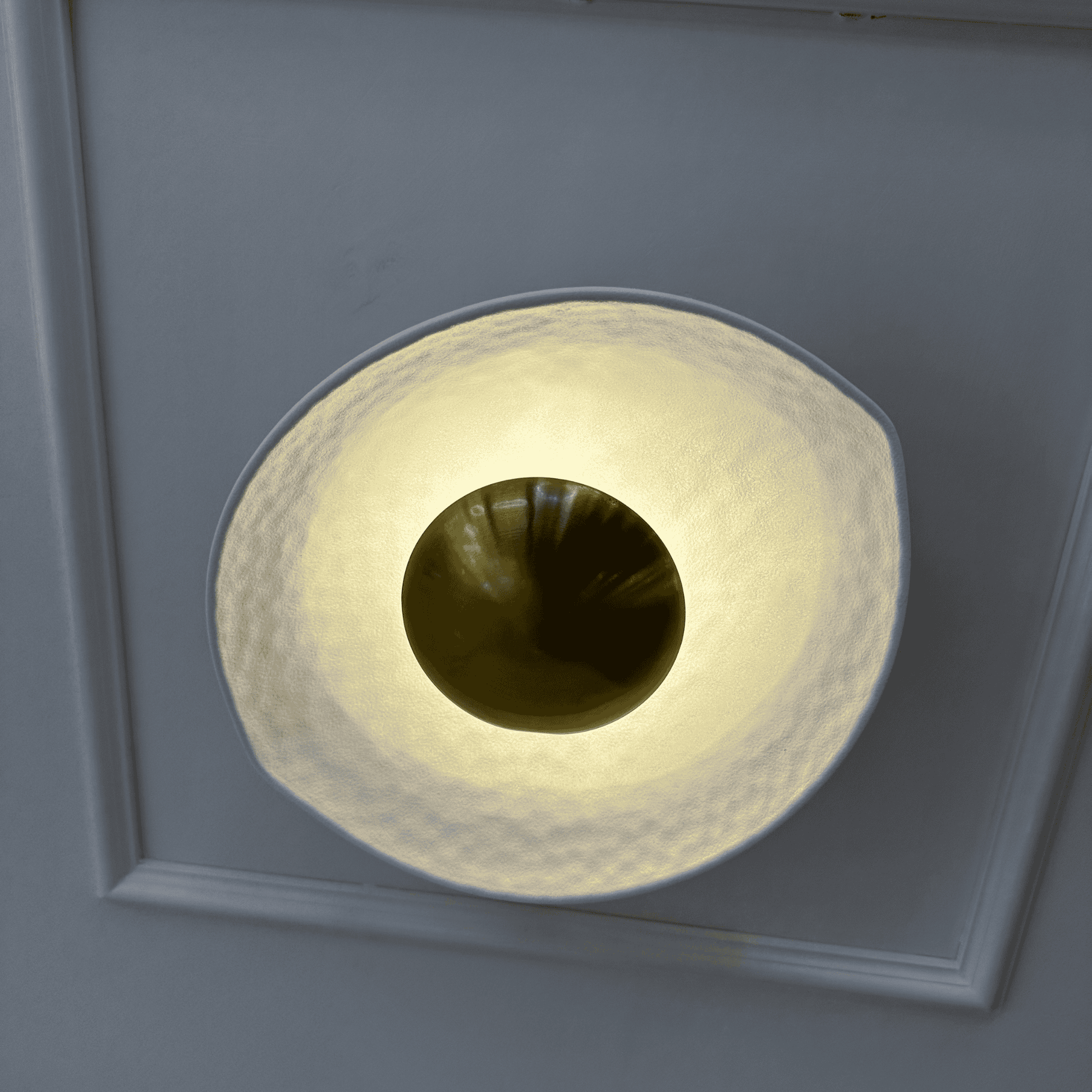 Close-up of a white and gold deco wall sconce with a round hammered finish and central golden dome.
