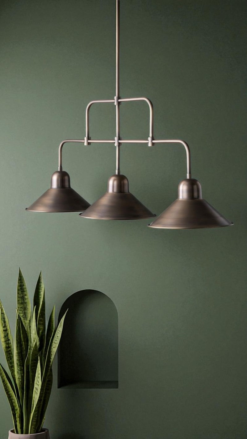 Bronze industrial triple pendant light mounted in front of a green wall with minimalist styling.