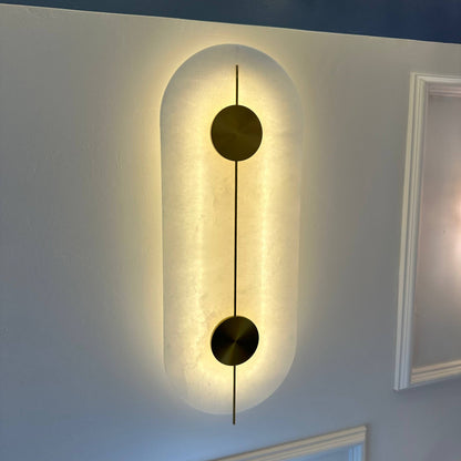 Modern alabaster wall light fixture with two brass discs and backlit glow for ambient interior lighting.