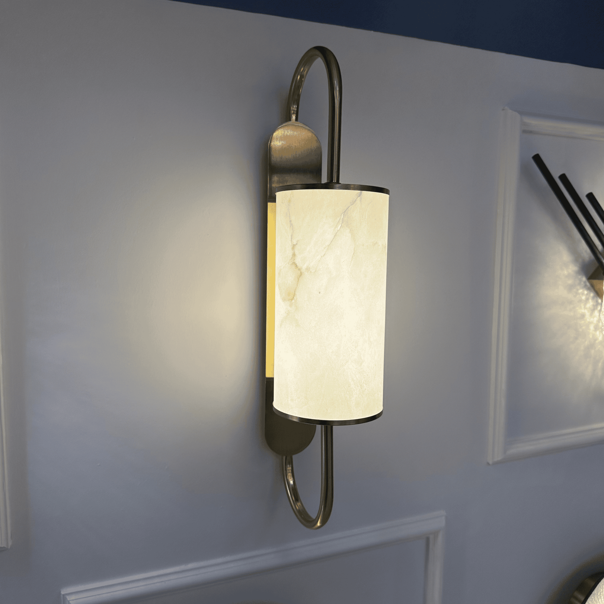 Modern alabaster and brass wall sconce glowing with soft light on an interior wall.