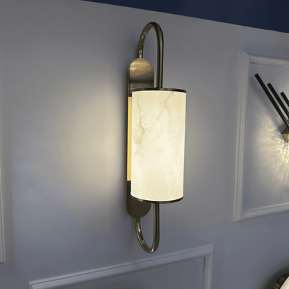 Modern alabaster and brass wall sconce glowing with soft light on an interior wall.