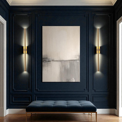 Modern brass wall sconces on dark navy paneled walls with a minimalist painting and bench in a contemporary entryway.