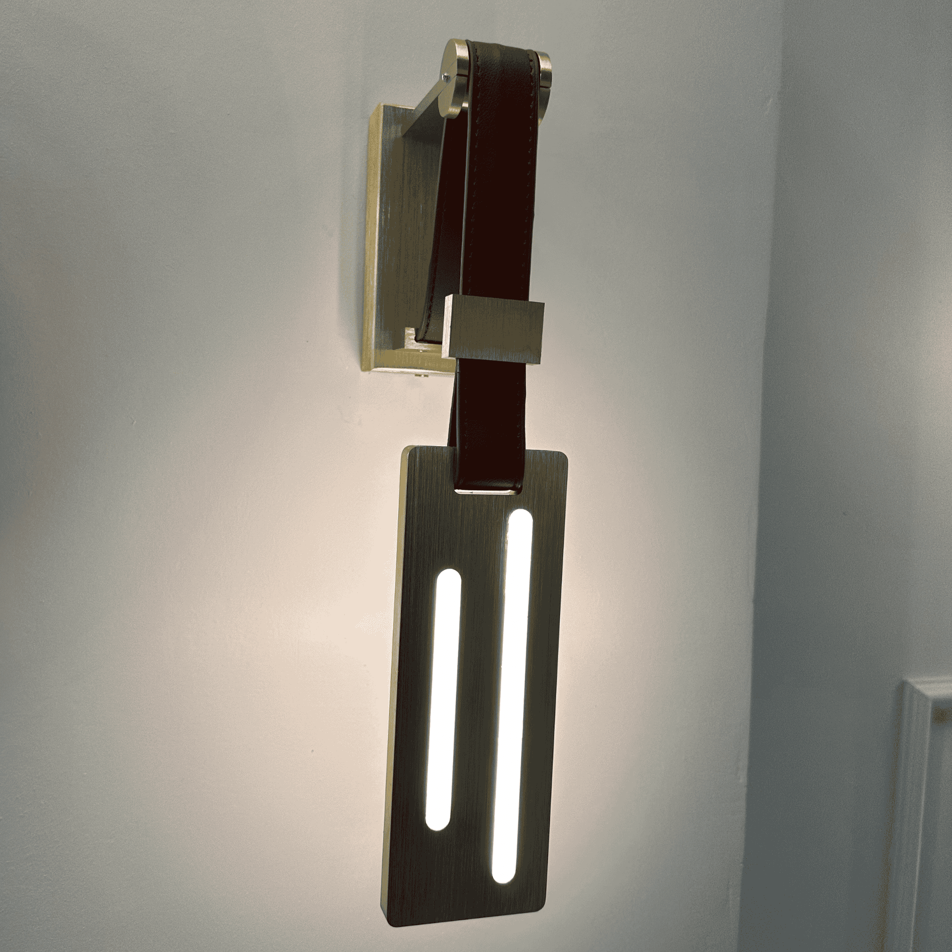 Modern leather wall sconce with vertical LED strip lights mounted on a brushed brass plate