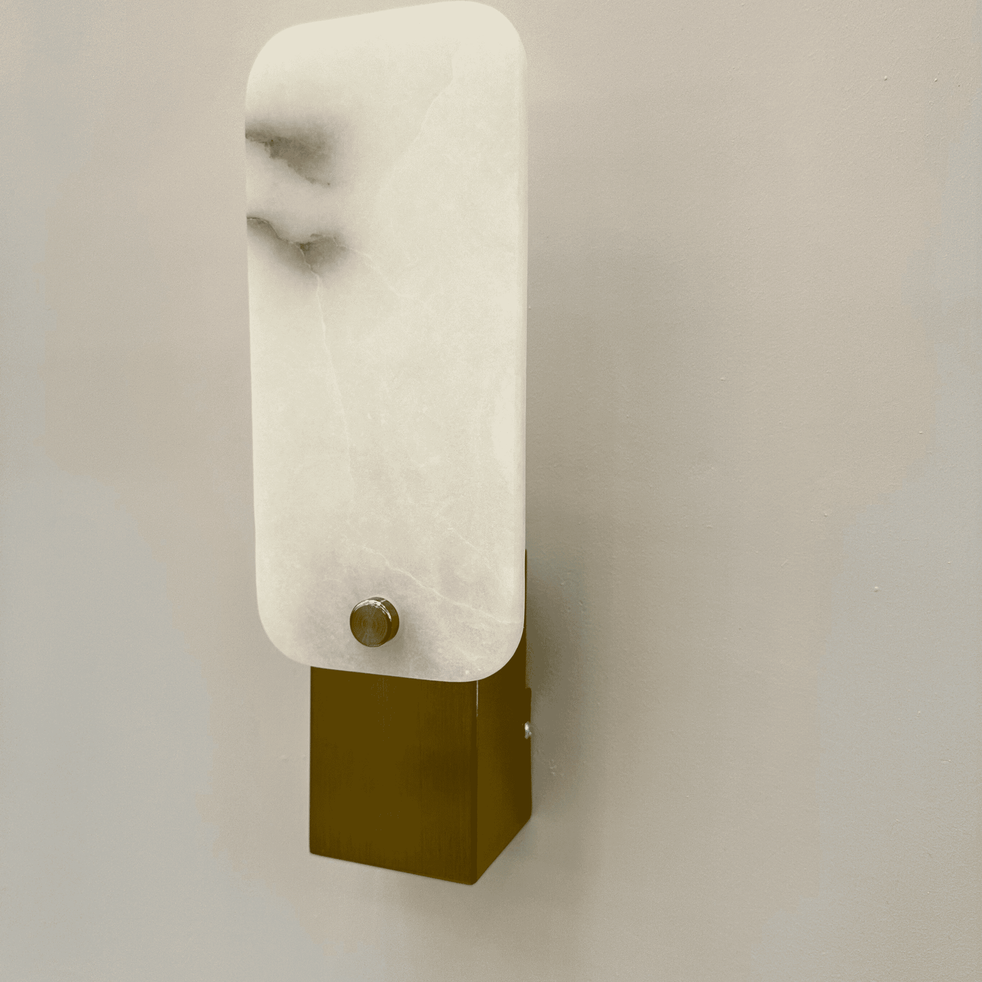 Angled view of modern square marble sconce with white stone face and brass detailing.