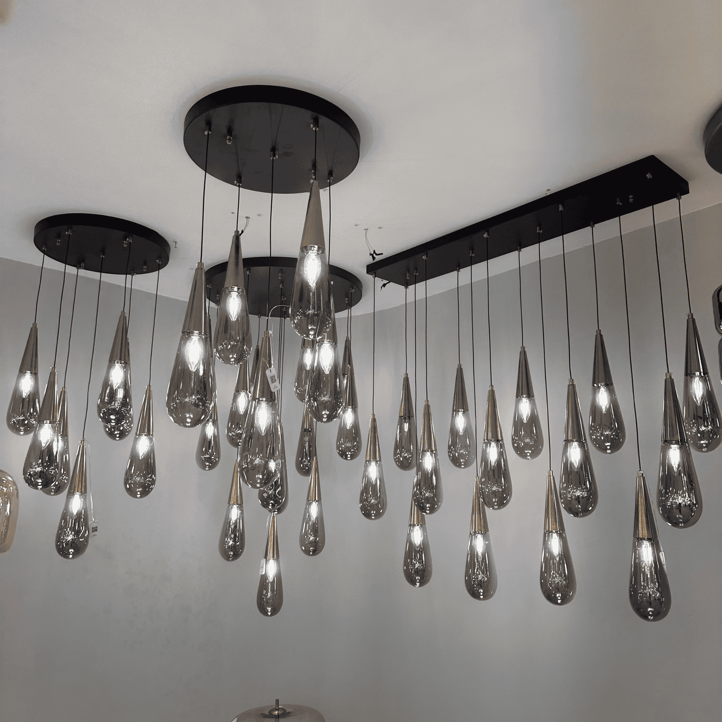 Cluster of teardrop-shaped glass pendant lights with black ceiling mounts, ideal for modern interior lighting.