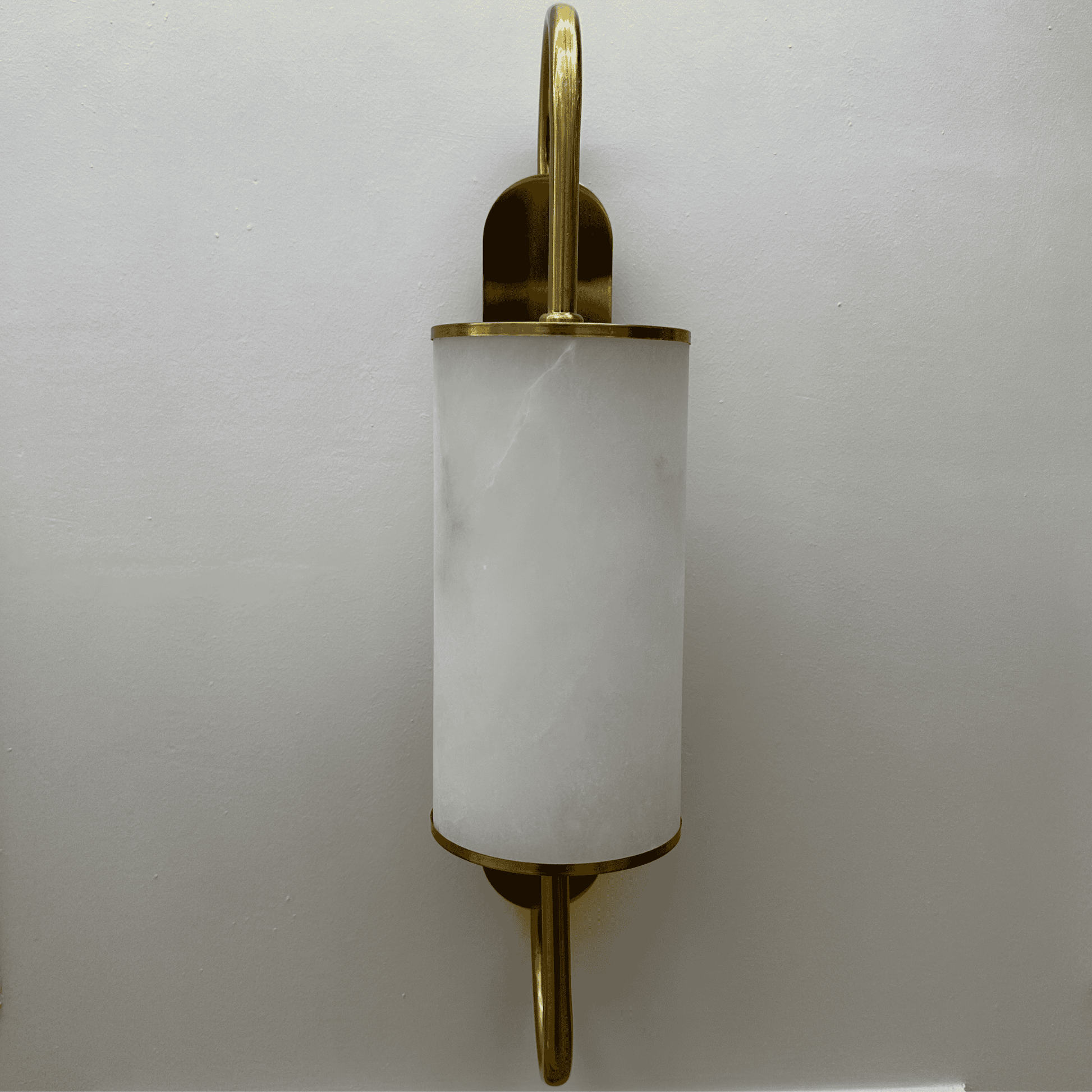 Modern wall sconce with a brass frame and cylindrical alabaster shade mounted on a light wall.