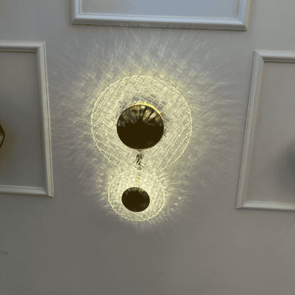 Modern brass and clear glass wall sconce casting patterned light on an entryway wall with classic molding.
