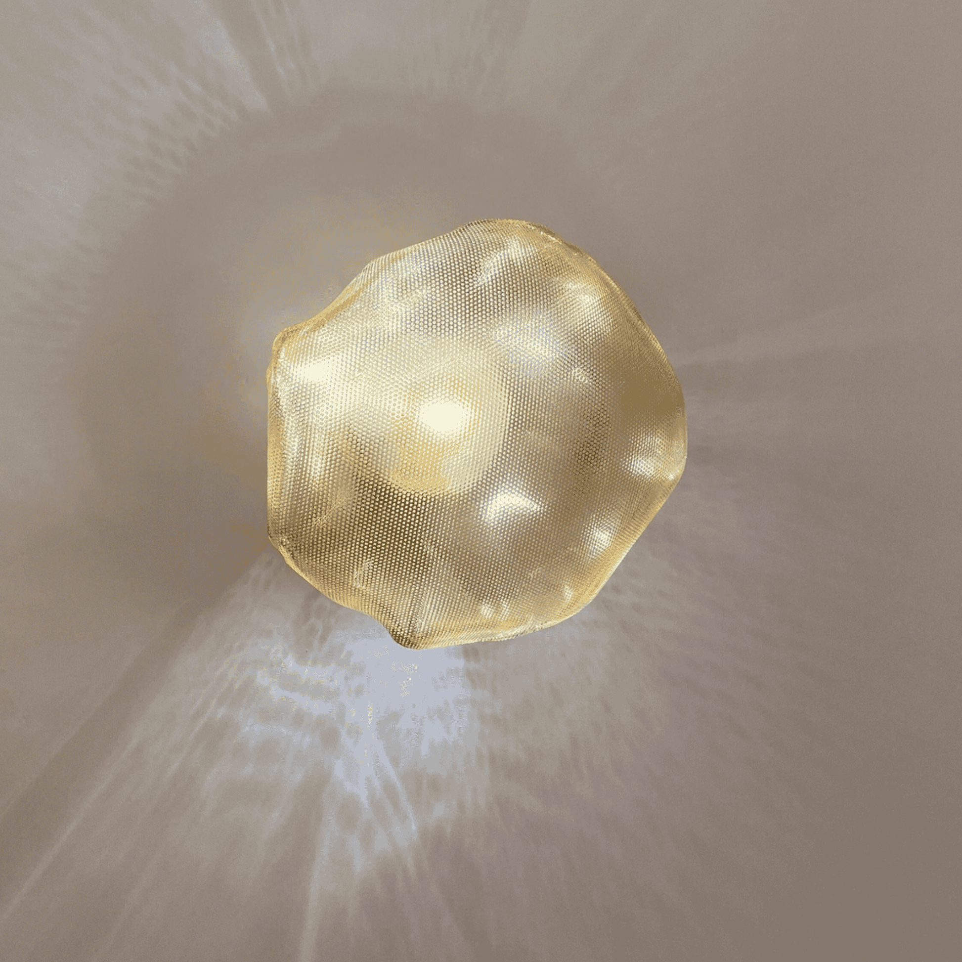 Organic-shaped glass wall sconce emits warm ambient light and textured shadows against a neutral backdrop.