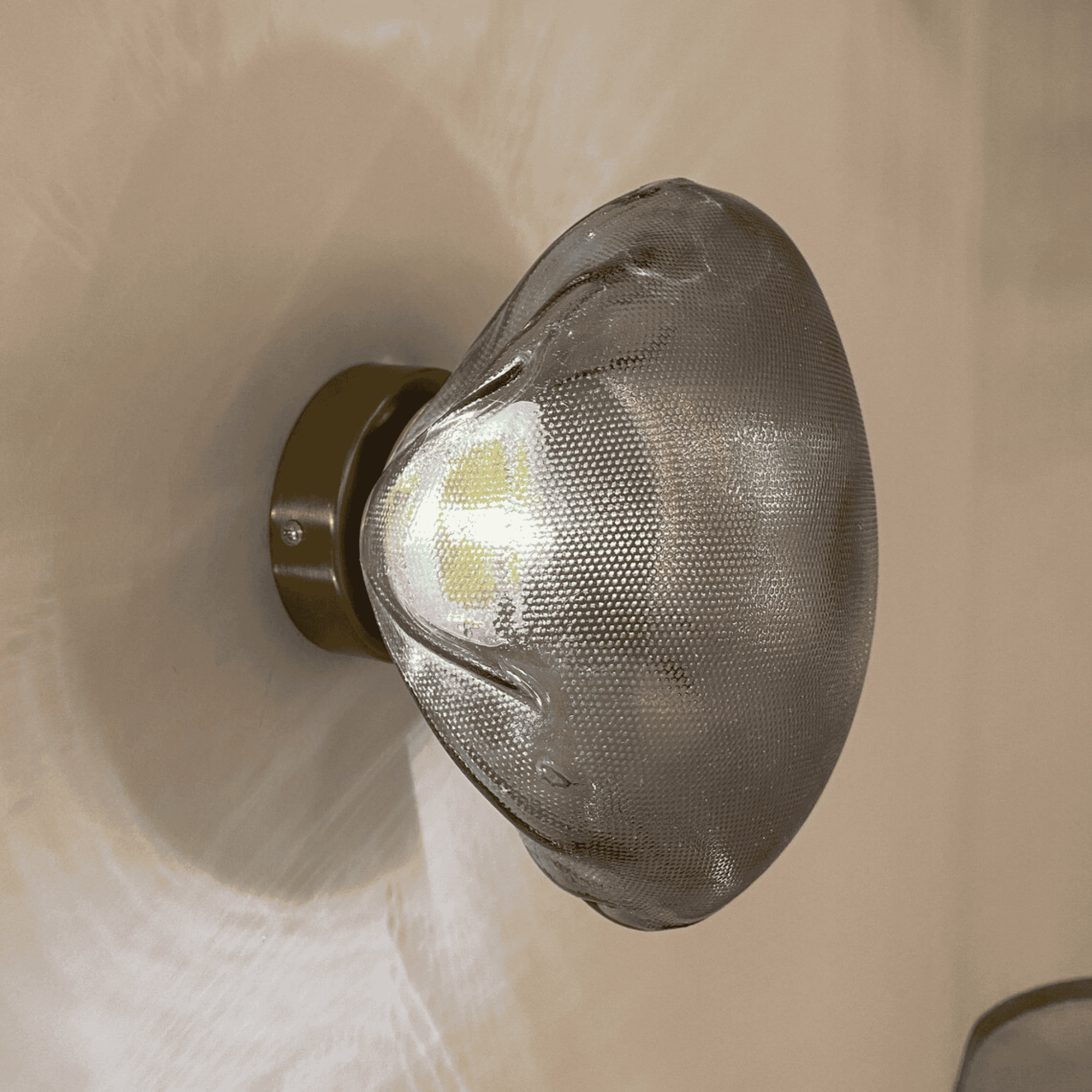 Smoky organic glass wall sconce on bronze base delivers ambient lighting with sculptural impact.