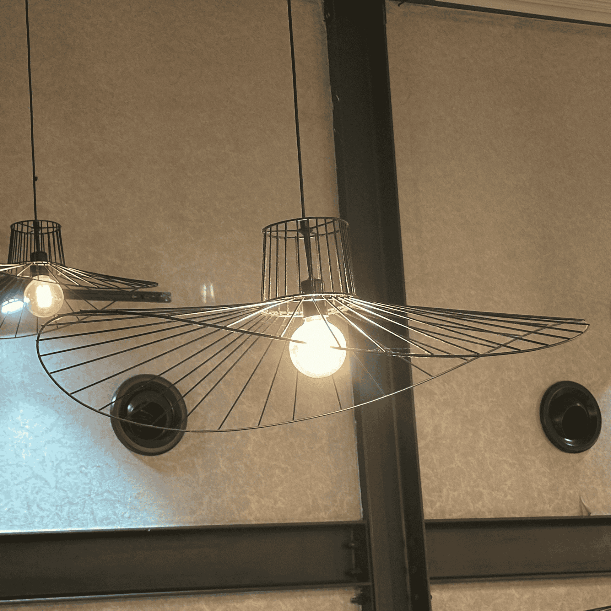 Overlapping straw hat pendant lights with wire shades illuminating a textured wall.
