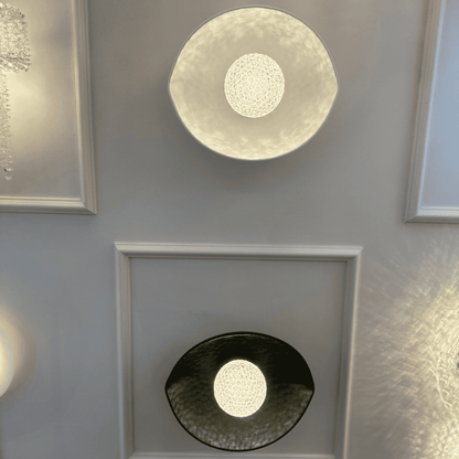 Two plexiglass LED wall sconces in black and white emit soft diffused lighting, mounted on a decorative paneled wall.