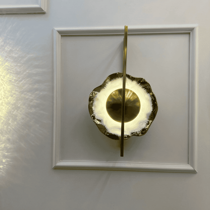 Fluted porcelain wall sconce with brass frame and warm halo lighting mounted on a paneled wall.