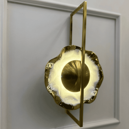 Side angle of porcelain wall sconce with sculptural brass frame and soft white lighting.