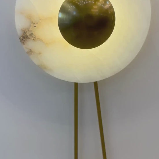 Alabaster wall sconce with a round brass disc and soft backlighting mounted on a paneled wall.