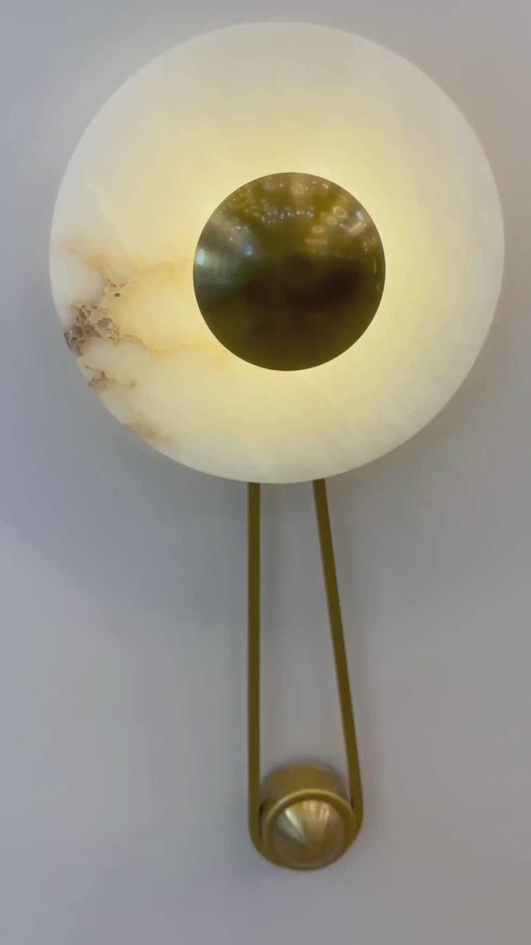 Alabaster wall sconce with a round brass disc and soft backlighting mounted on a paneled wall.