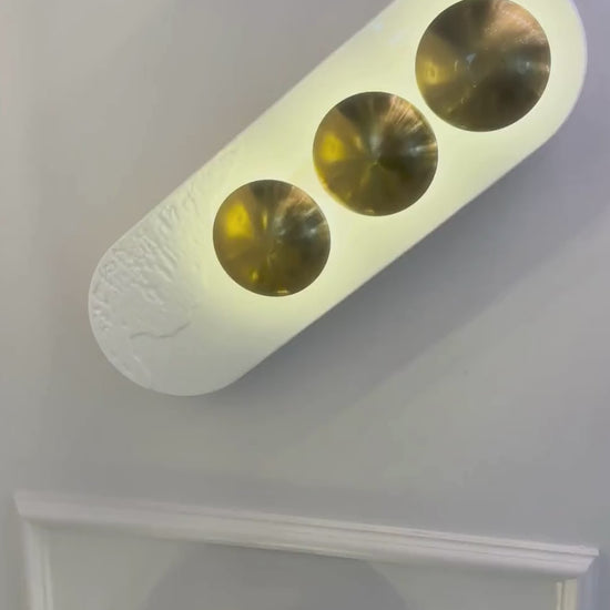 Vertical minimalist LED wall sconce with two brass accents and white resin for modern interiors.