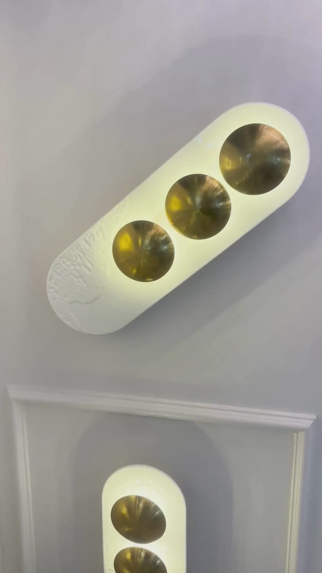 Vertical minimalist LED wall sconce with two brass accents and white resin for modern interiors.