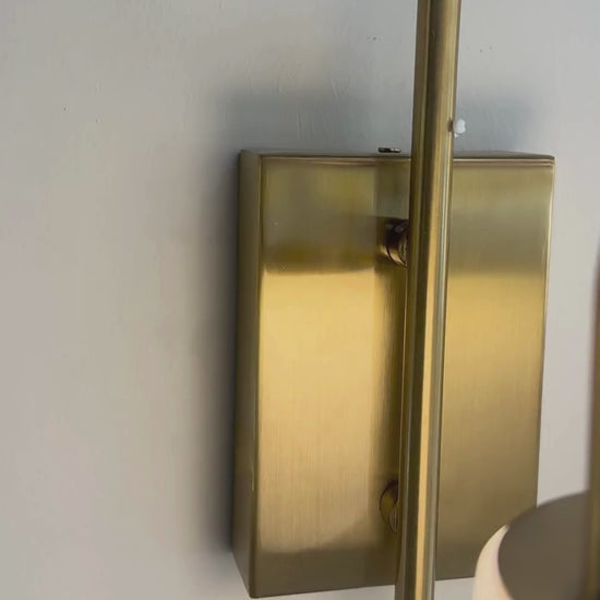 Modern brass and alabaster marble wall sconce with curved arm and soft lighting.
